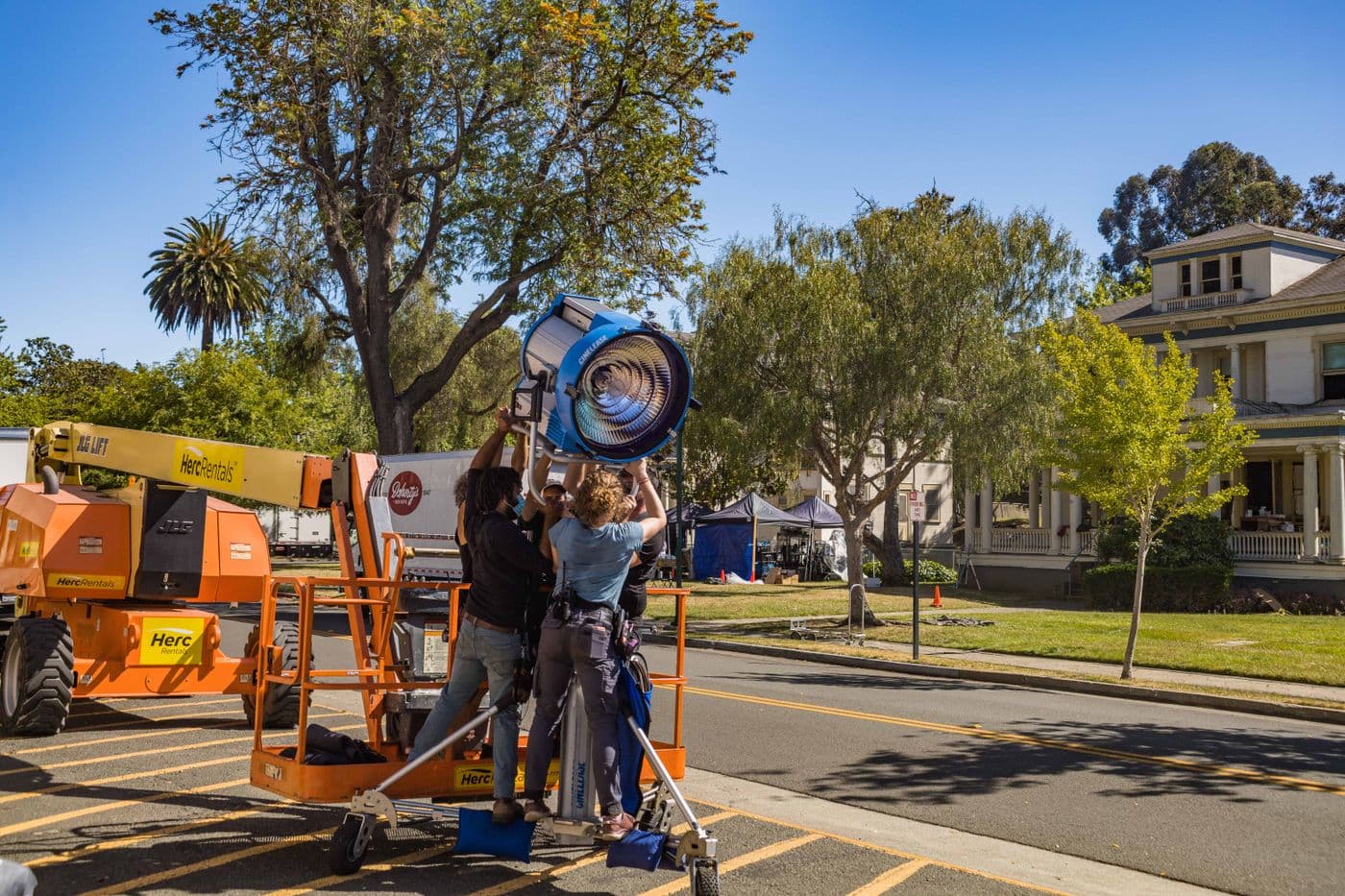 Crew members rigging a large lamp on a cherry picker at a street location