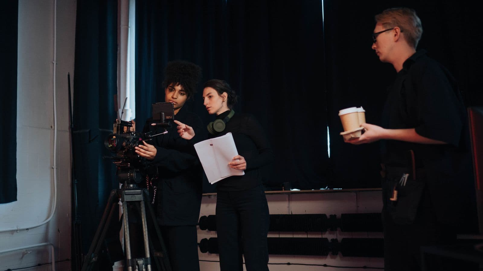 Film crew around a camera on set, one crew member holding printed script pages