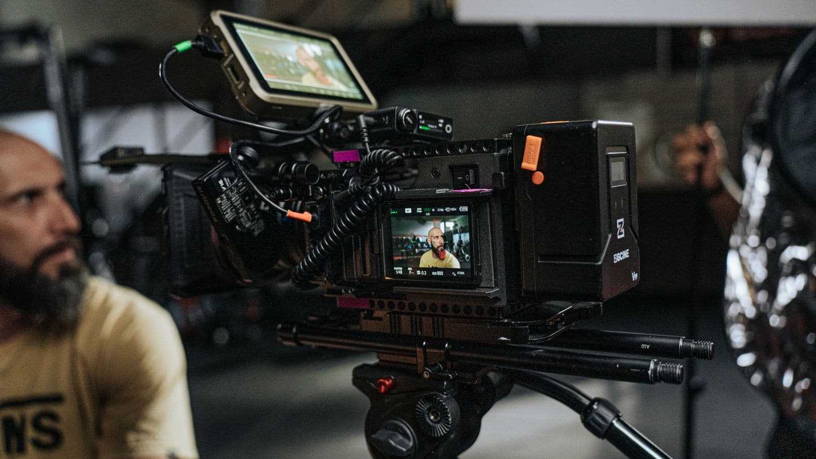 Caméra de cinéma équipée sur pied, sur un plateau de tournage, avec un membre de l'équipe au second plan
