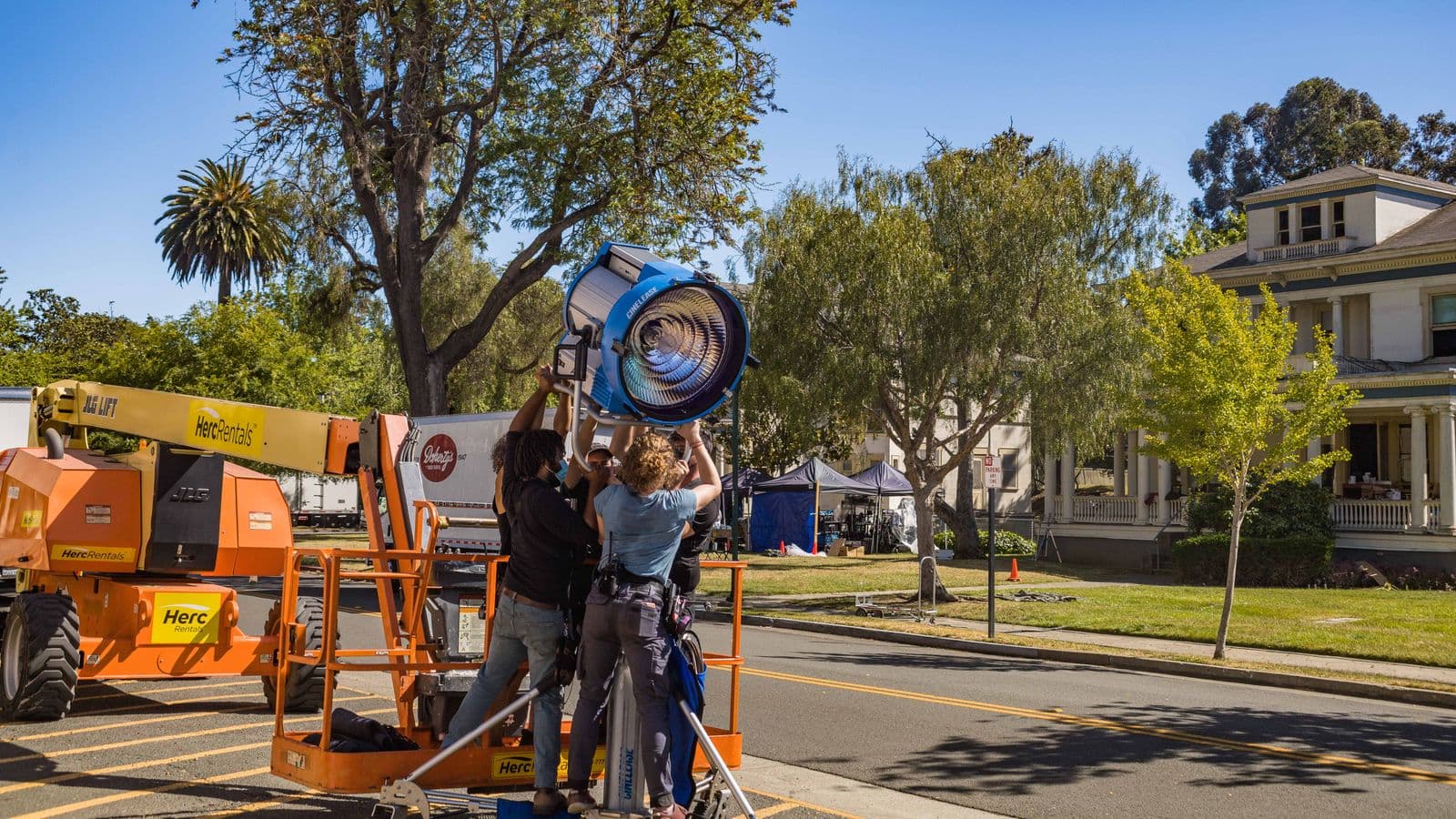 Three crew members rigging a large film light on a cherry picker during an exterior location shoot