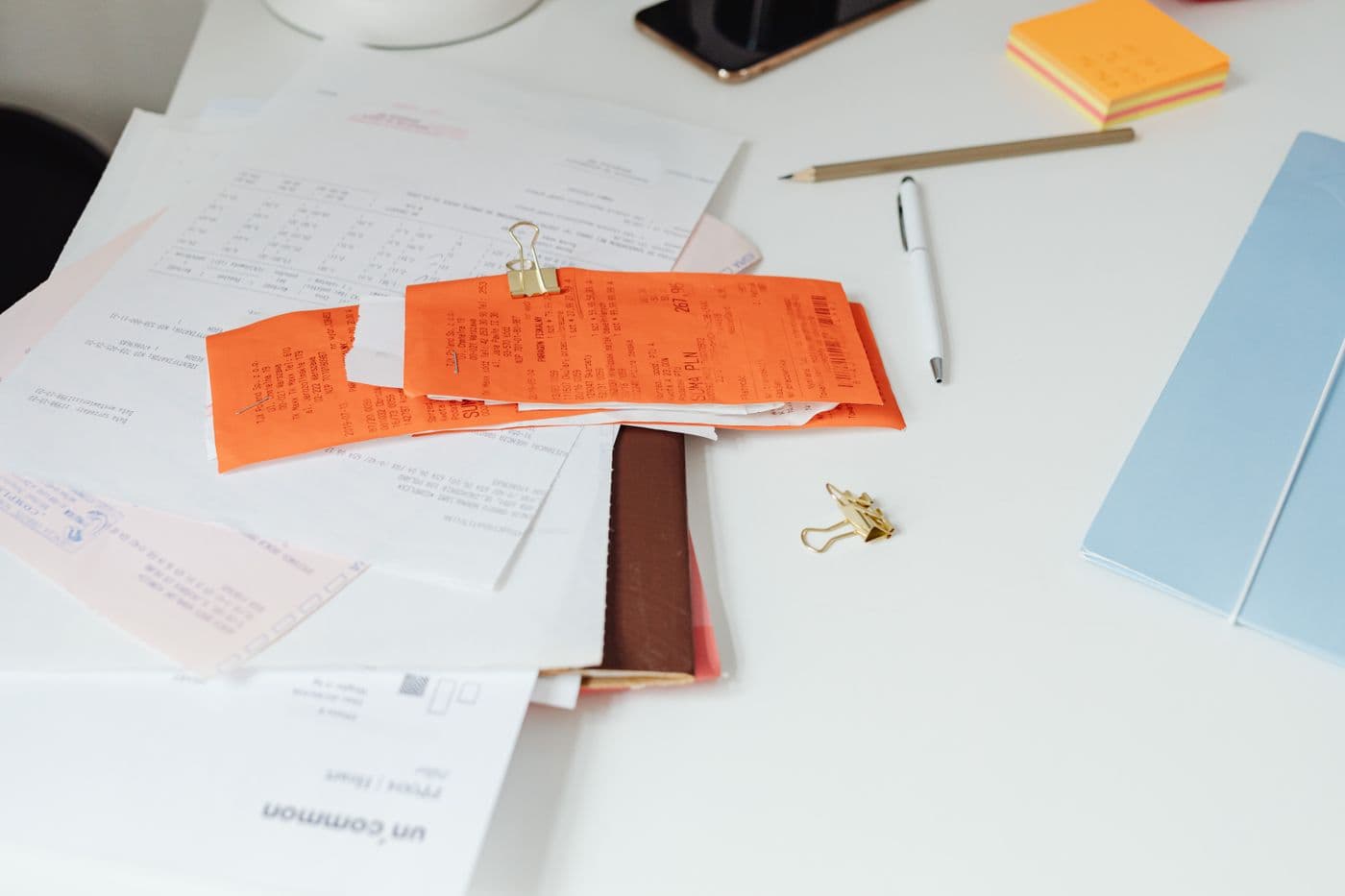 Des justificatifs et des factures empilés sur un bureau clair, à côté d'un stylo et d'un carnet