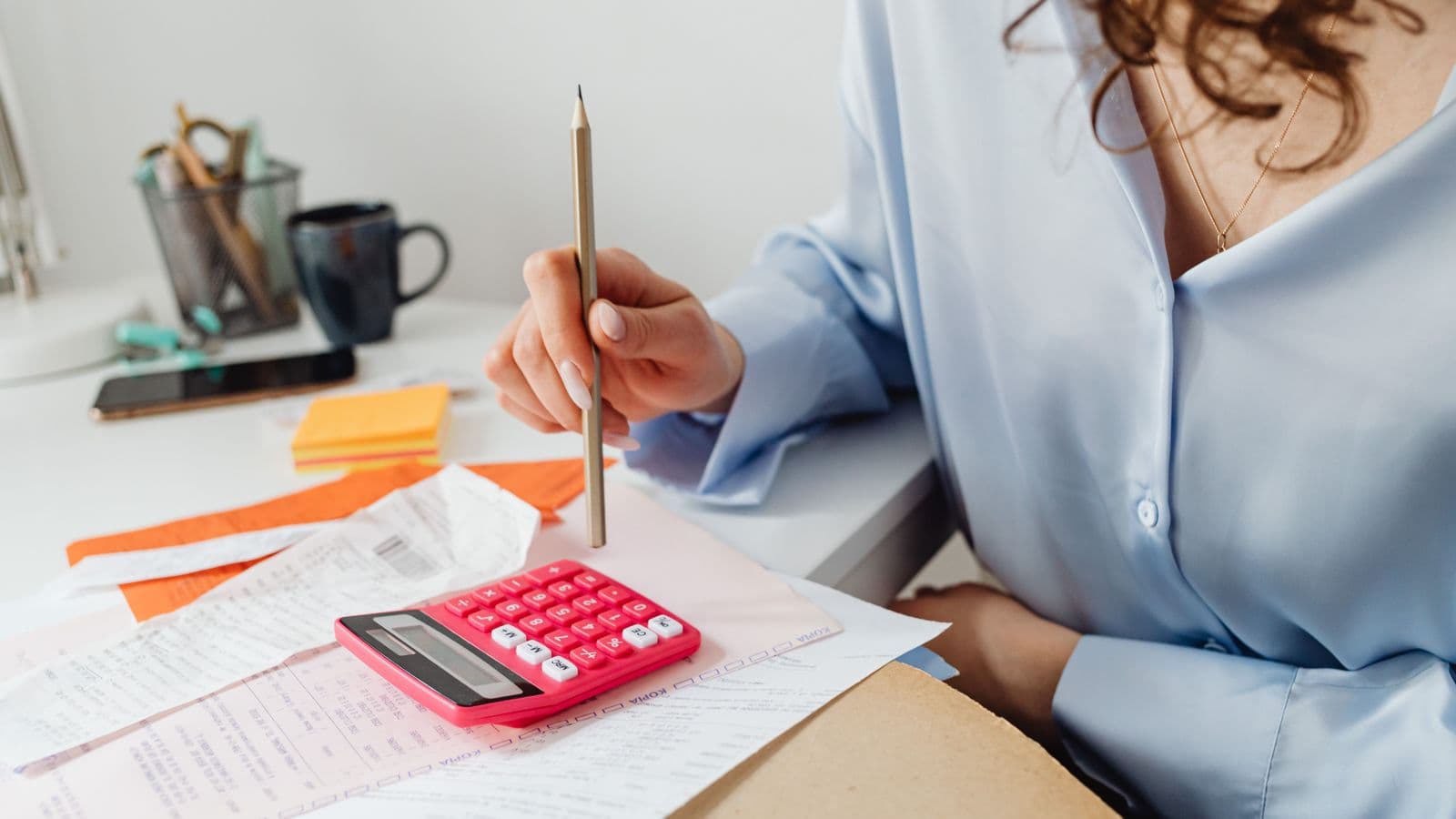 Une personne calcule des dépenses avec une calculatrice, des factures et des justificatifs sur son bureau