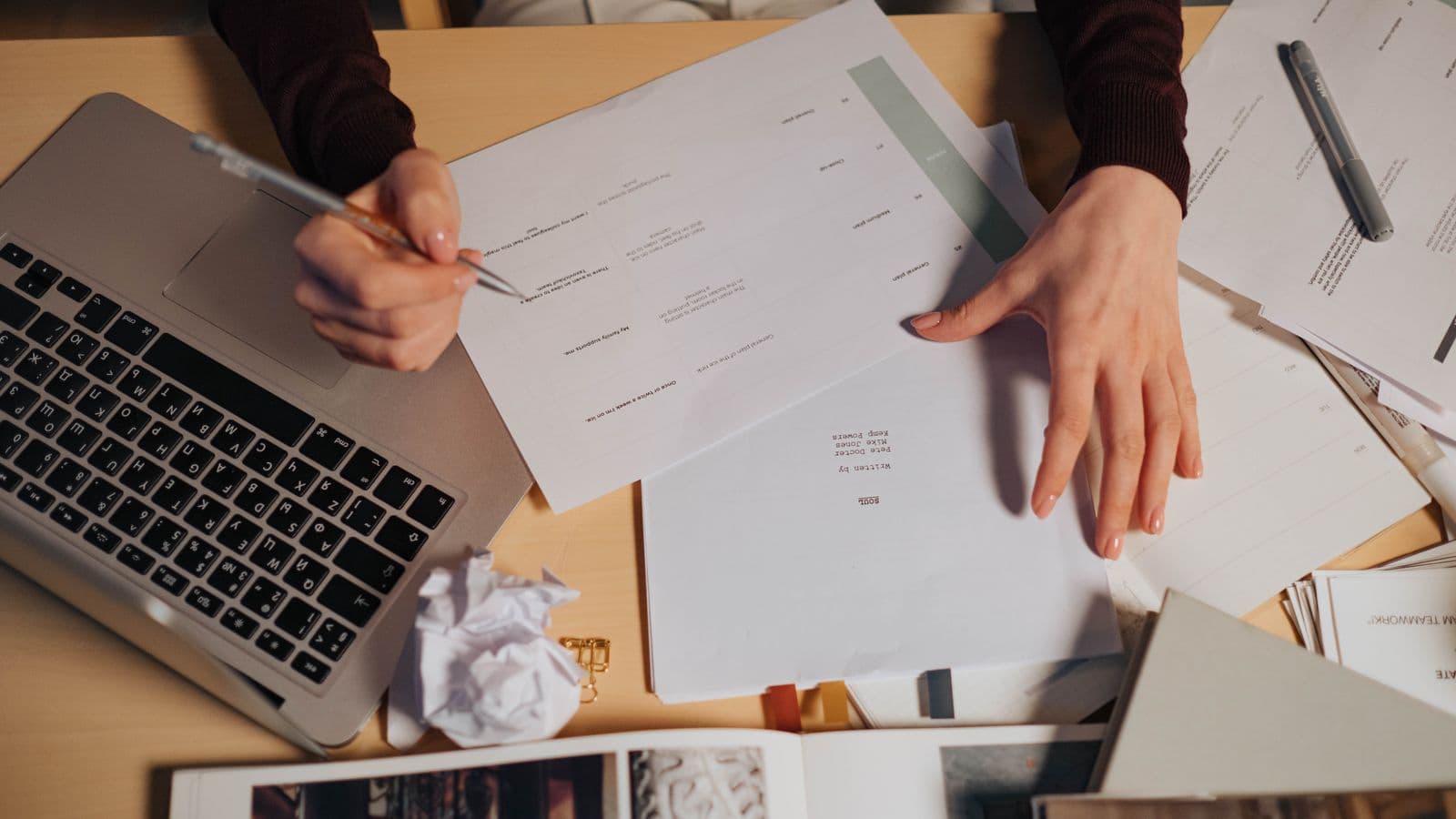 Une personne annote un planning papier au milieu de documents de production et d'un ordinateur portable