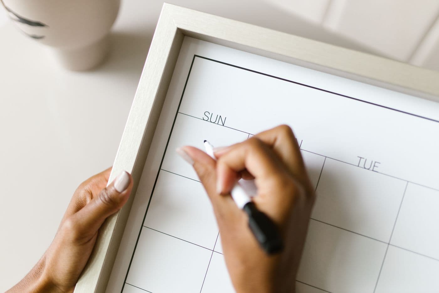 A hand marking up a monthly wall calendar with a felt pen