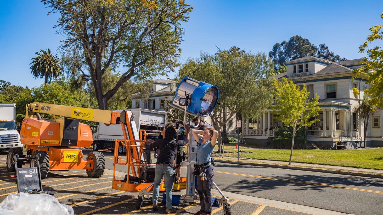 Une équipe installe un projecteur sur une chaussée, devant un camion technique et une nacelle de location