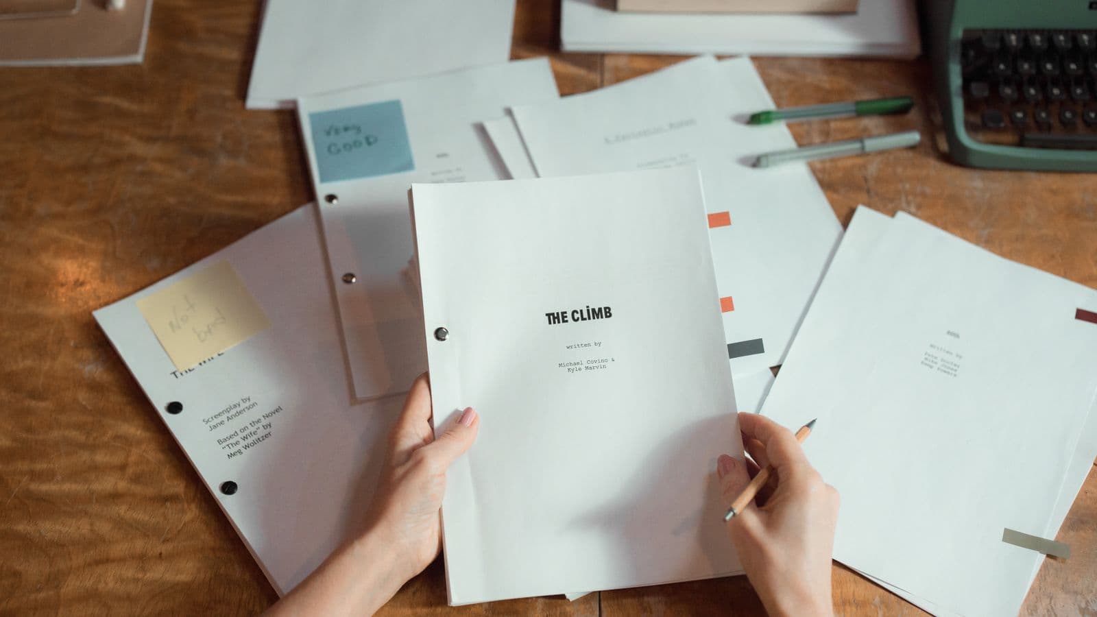 Hands holding screenplay pages on a wooden desk next to a typewriter